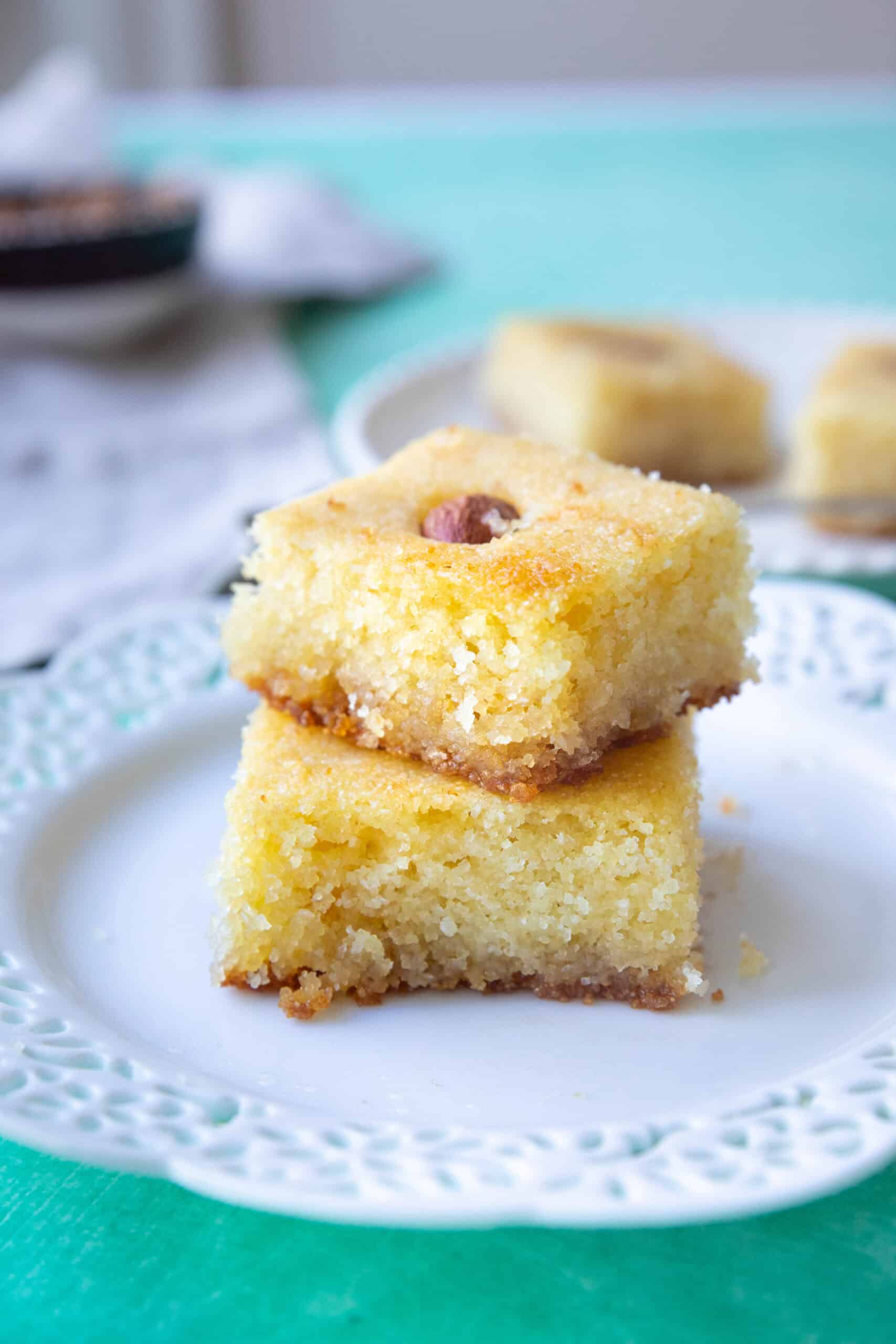 Basbousa (Middle Eastern Semolina Cake) fluffy and moist basbousa (semolina cake) served in a white dish with one piece on top of the other