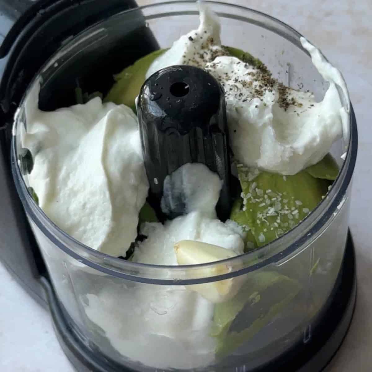 greek yogurt and pepper are added to avocado slices and parsley in the food possessor
