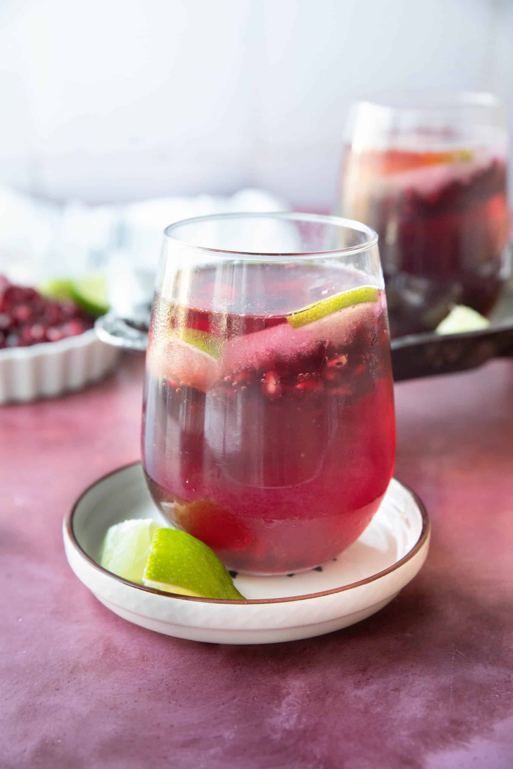 Pomegranate Mocktail pomegranate mocktail served in a transparent glass on a white dish with lime wedge next to it