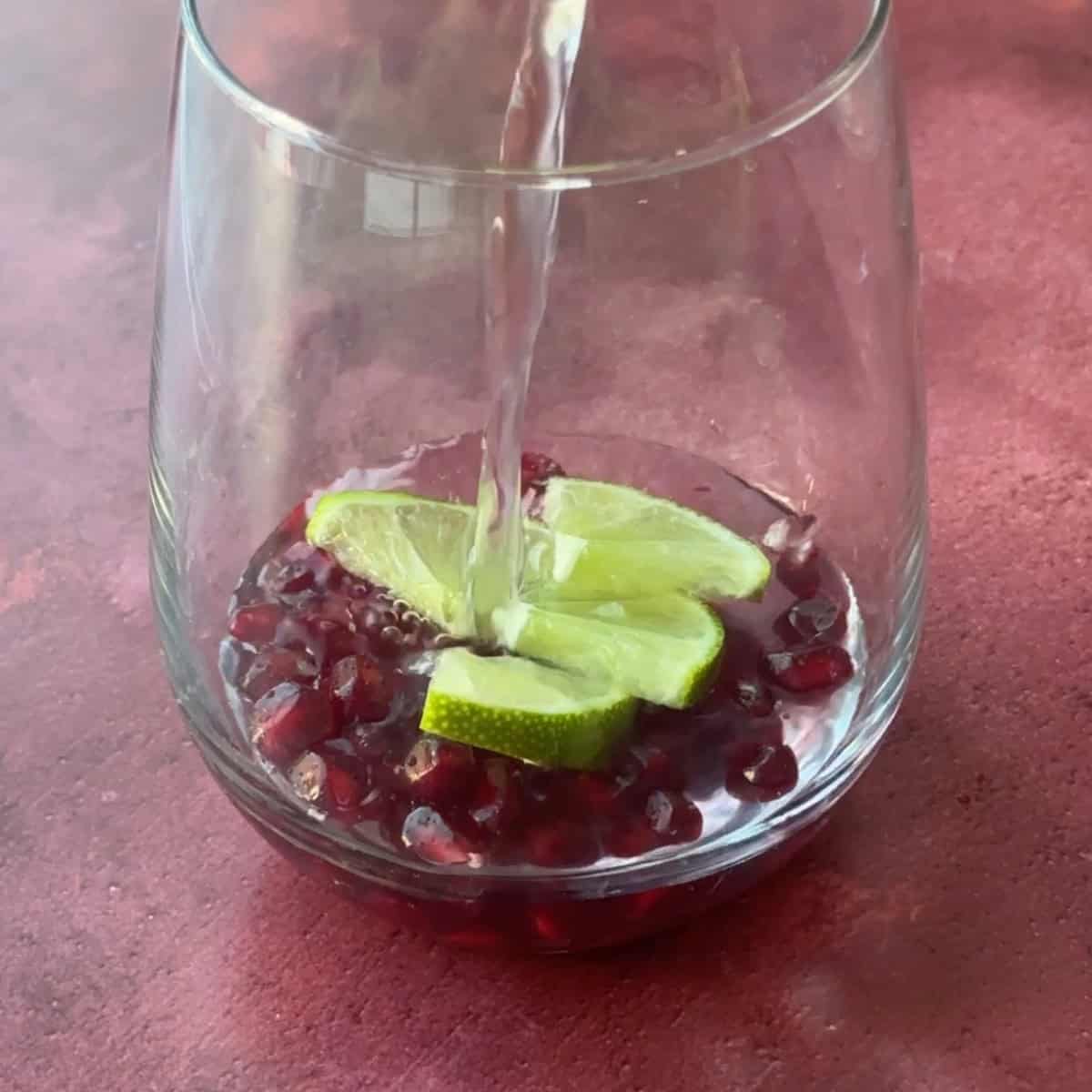 How to Make Pomegranate Mocktails fill glasses with pomegranate arils and lime and pour water over them