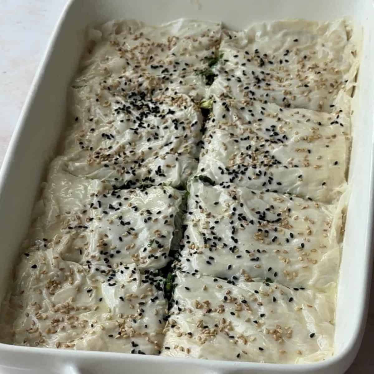 How to Make Spinach Feta Borek Top layer of phyllo dough added to the baking pan, with the surface brushed with sauce and sprinkled with sesame and nigella seeds, with the layers sliced.
