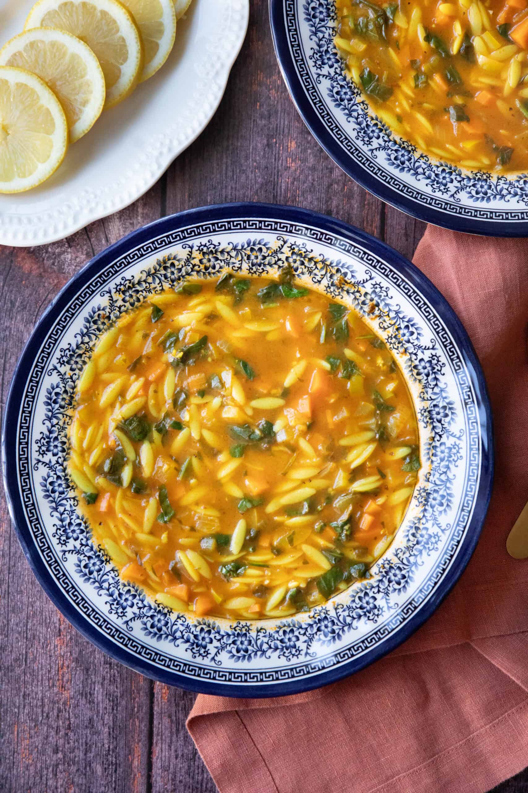 two Bowl of Mediterranean vegetable orzo soup topped with fresh spinach and served with lemon wedges.