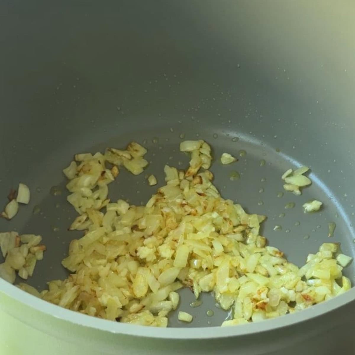 Diced onion and garlic sautéing in olive oil for Mediterranean vegetable orzo soup.