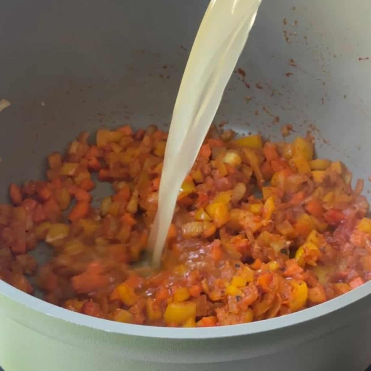 Pouring broth into the pot to create the base of Mediterranean vegetable orzo soup.