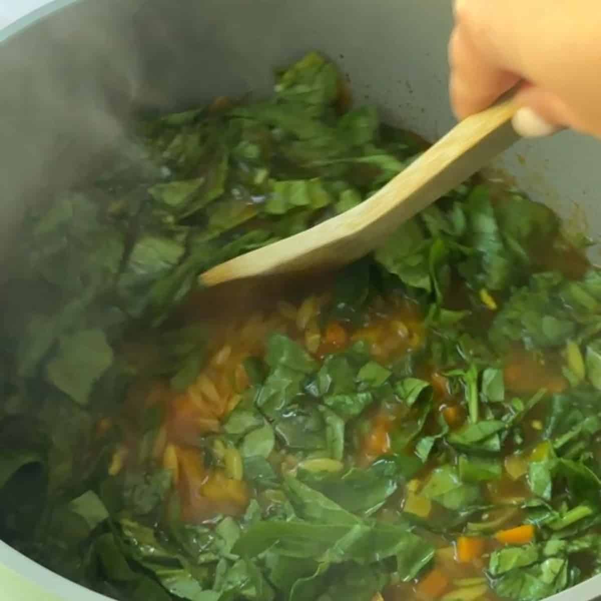 Chopped spinach and a squeeze of lemon juice added to finish the vegetable orzo soup.