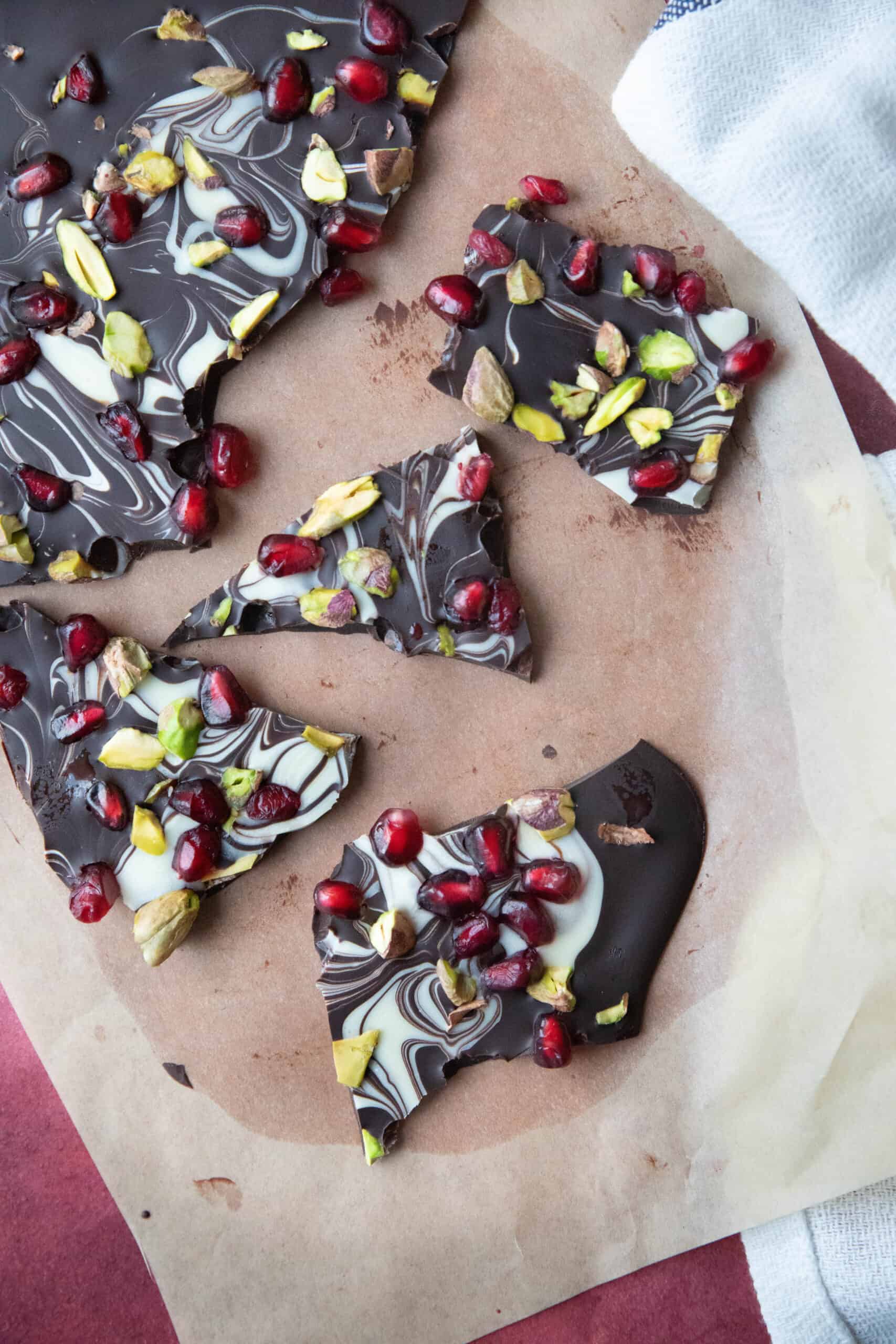 Pomegranate Chocolate Bark A white plate filled with large pieces of chocolate bark topped with pistachios and pomegranate seeds.