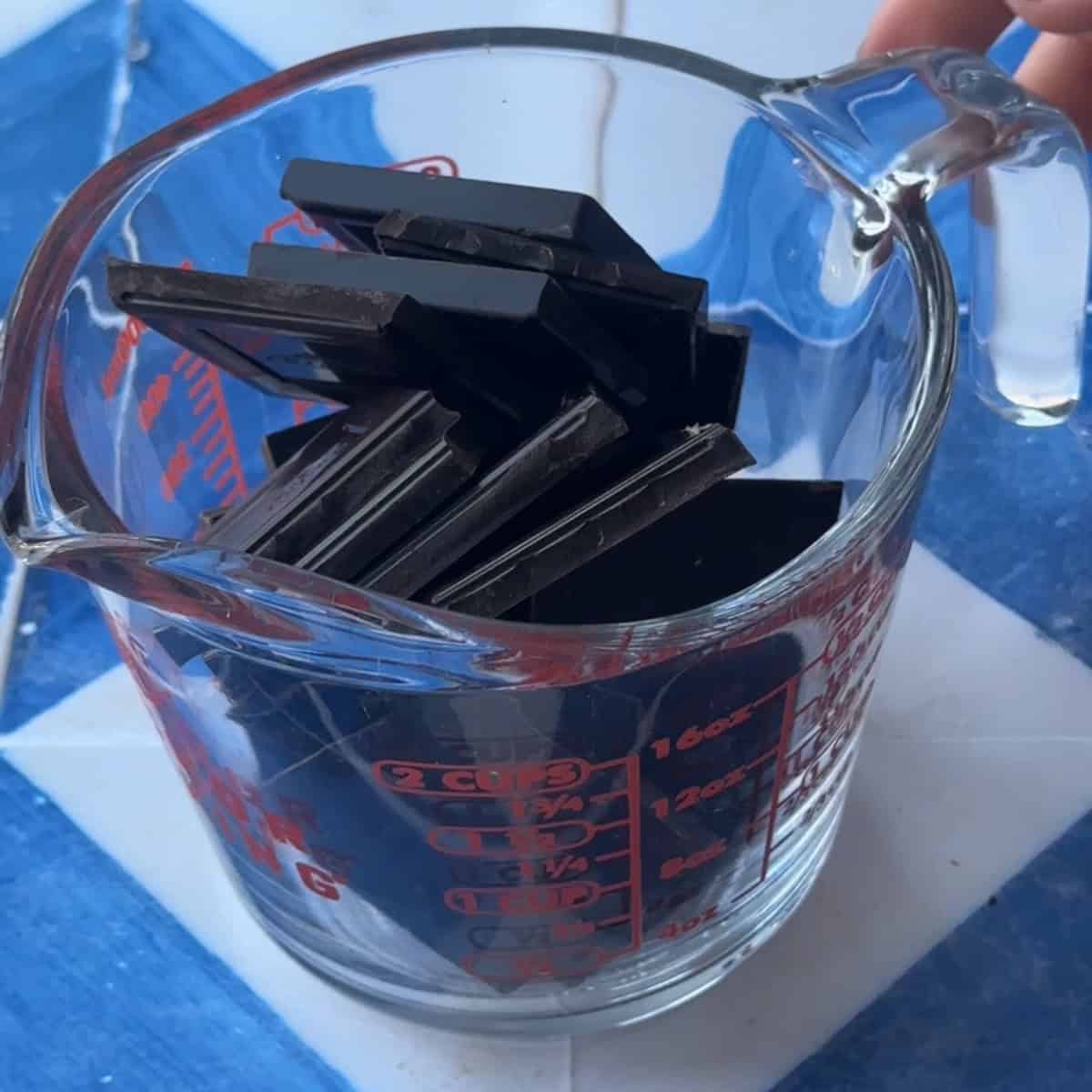 A measuring cup filled with pieces of dark chocolate.