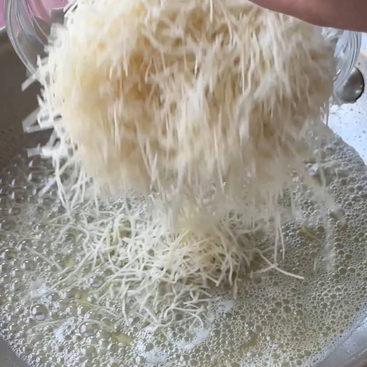 Adding shredded kataifi dough to the pan that has butter.