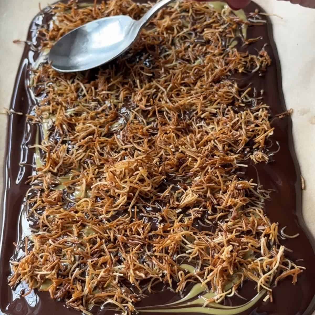 Placing golden brown kataifi dough to melted dark chocolate on parchment paper.