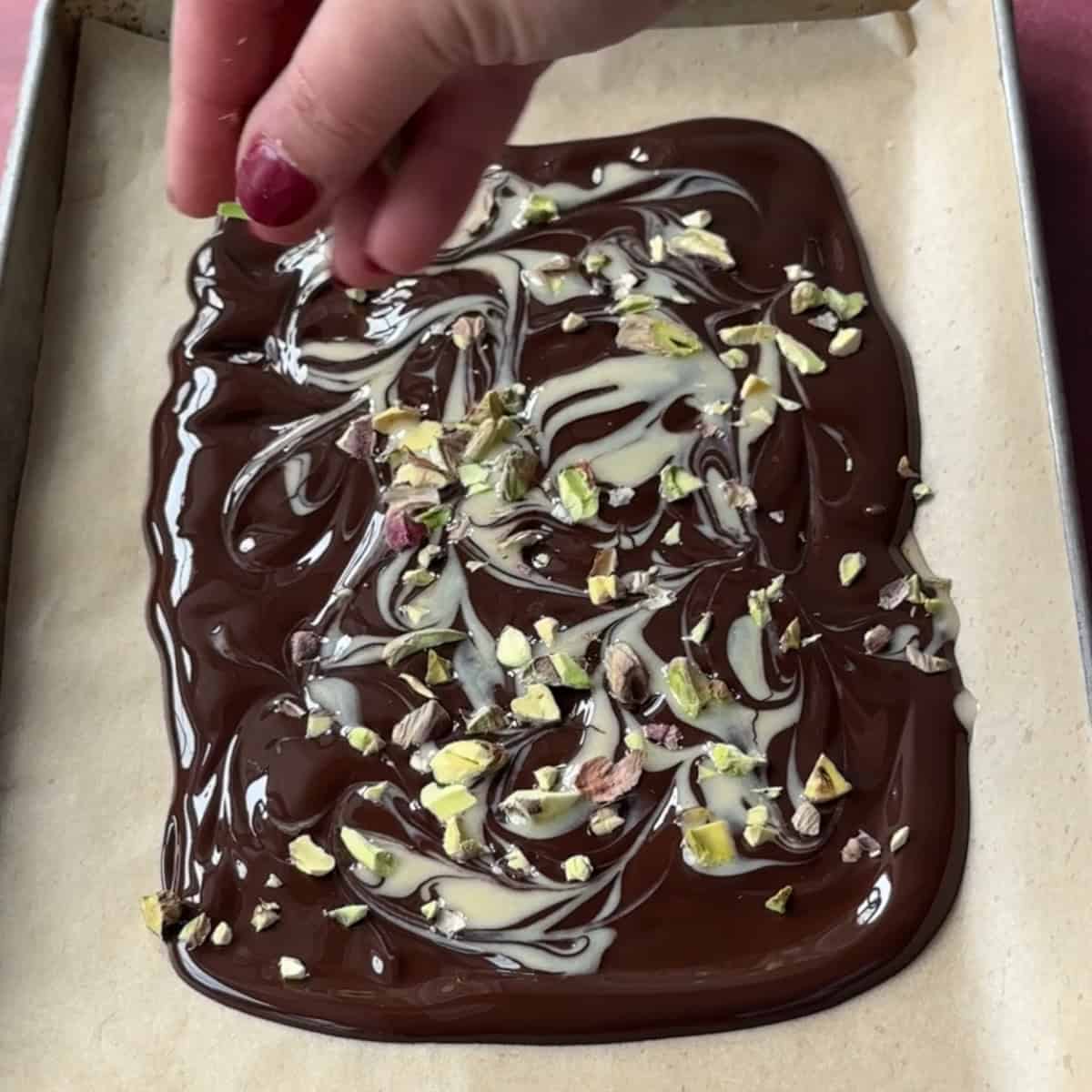Adding chopped pistachios to melted chocolate drizzled with tahini.