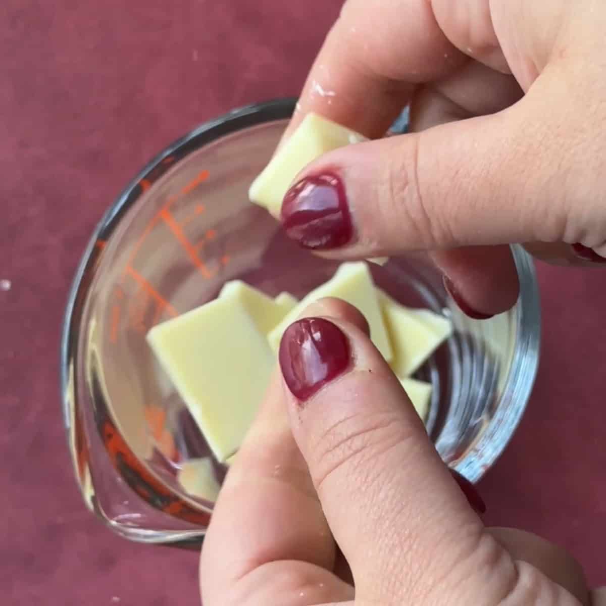 A hand breaking white chocolate to melt in a microwave.