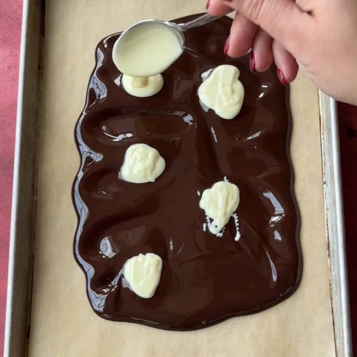 Adding melted white chocolate to melted dark chocolate on parchment paper.