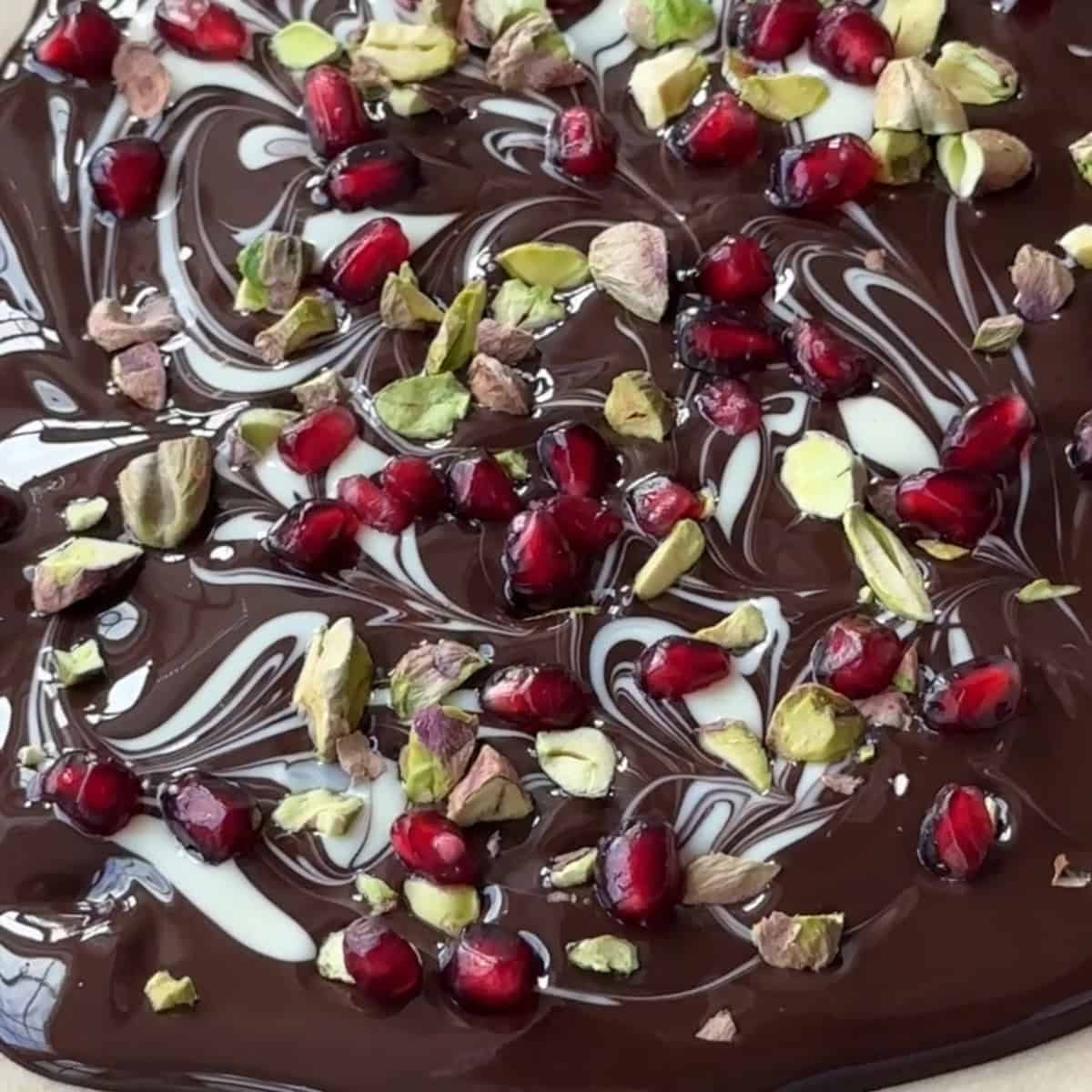 Melted chocolate on parchment paper topped with pistachios and pomegranate.
