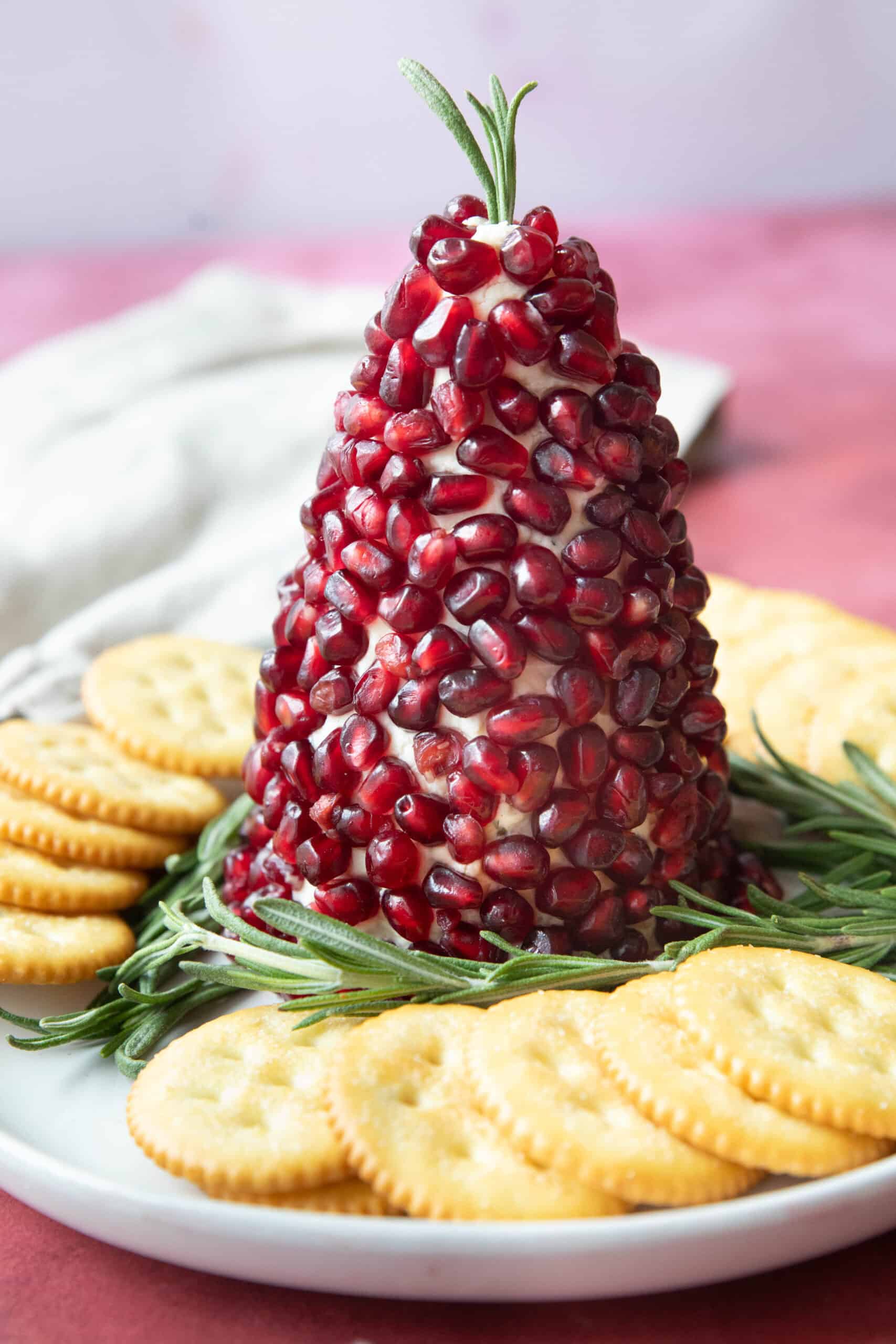 Christmas Tree Cheese Ball Christmas tree cheese ball served on a plate with sprigs of rosemary and crackers around it