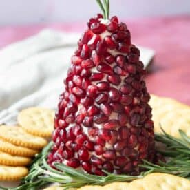 Christmas tree cheese ball served on a plate with sprigs of rosemary and crackers around it