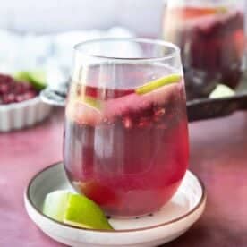 pomegranate mocktail served in a transparent glass on a white dish with lime wedge next to it