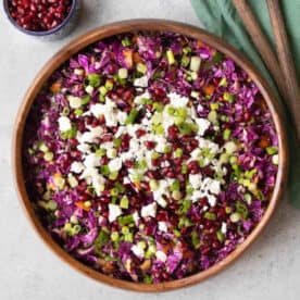 red cabbage pomegranate salad served in a wooden bowl with a small bowl of pomegranate arils in the background