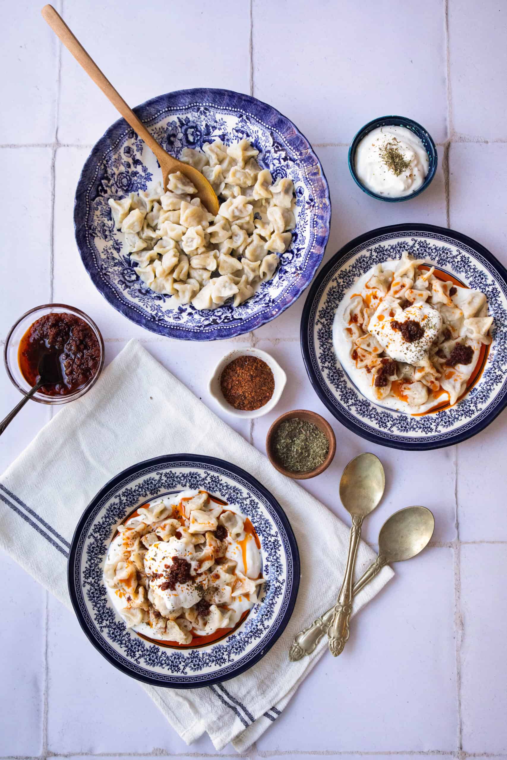 Manti with Ground Beef a bowl of manti placed next to two servings of manti derizzled with the garlicky yogurt sauce and the tomato sauce