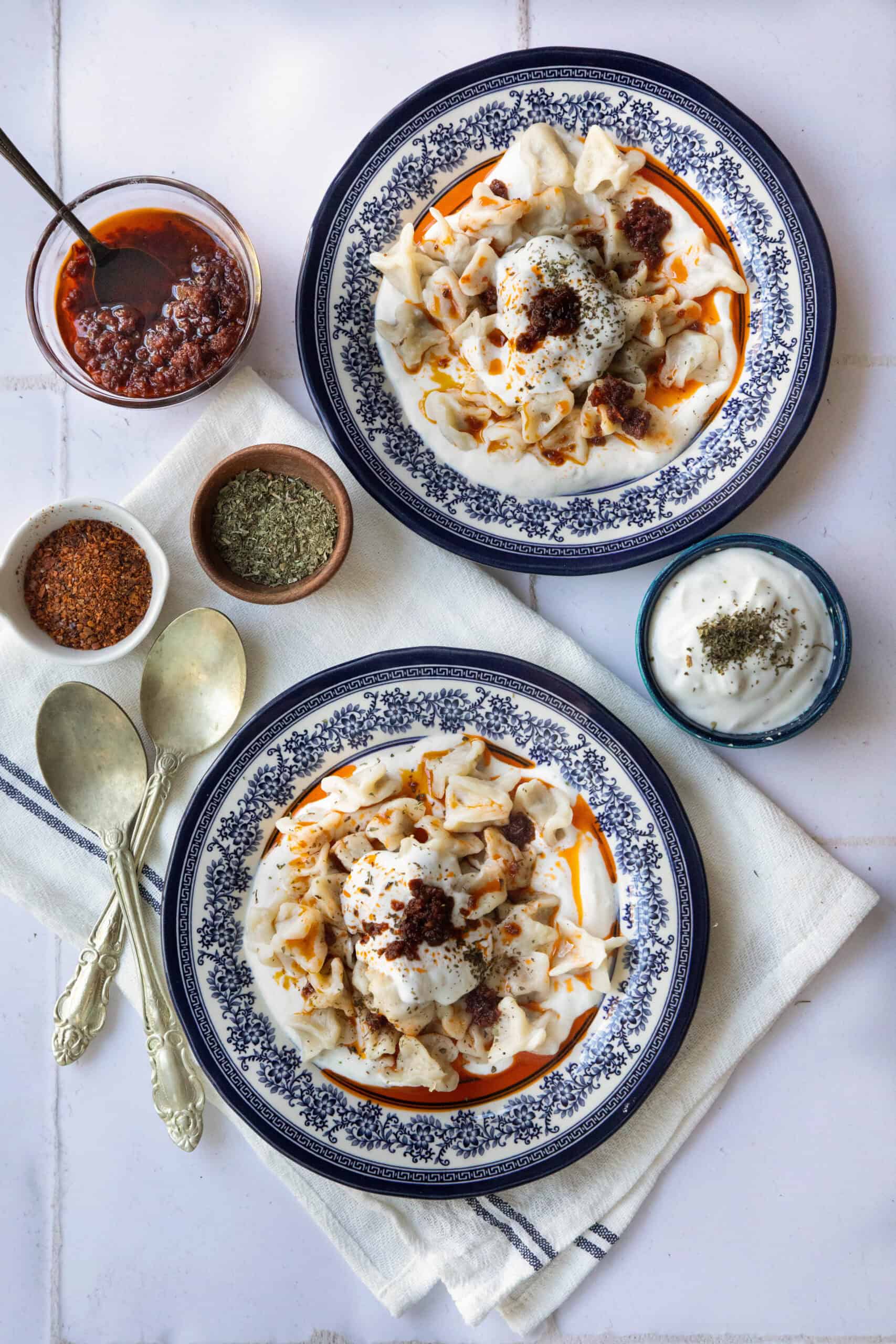 Homemade Manti two servings of manti topped with creamy garlicky yogurt and vibrant tomato butter sauce, garnished with dried mint and Aleppo pepper