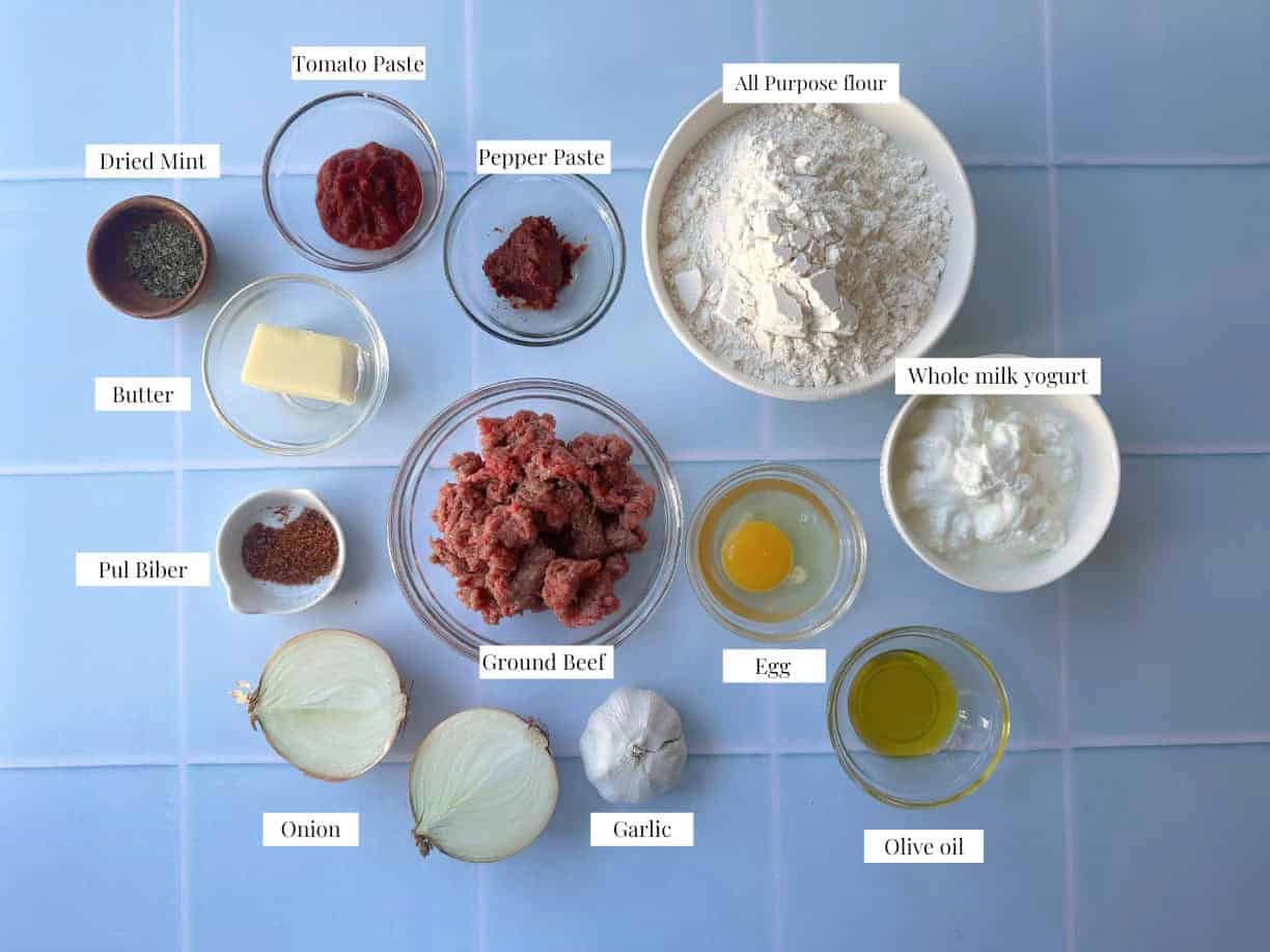 Manti Ingredients A collection of ingredients for Turkish manti, including flour, egg, water, and salt for the dough; ground beef, grated onion, salt, and Aleppo pepper for the filling; butter, olive oil, pepper paste, tomato paste, and Aleppo pepper for the tomato butter sauce; and yogurt, garlic, salt, and dried mint for the garlicky yogurt topping