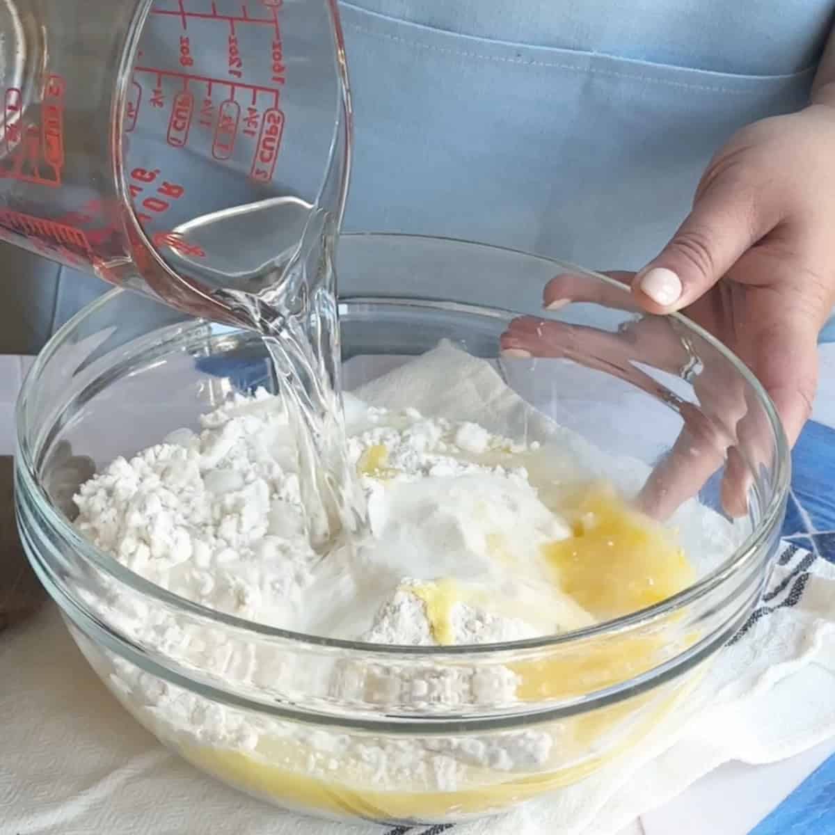 Manti Dough Ingredients A mixing bowl with flour, beaten egg, salt, and water being poured on them
