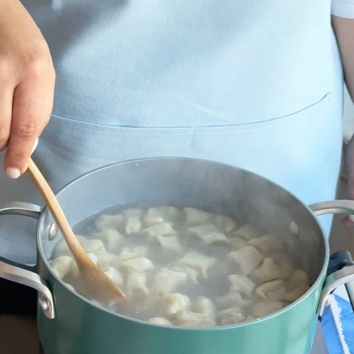 Boiling Manti A wooden spoon stirring the pot to prevent manti from sticking together as they cook.