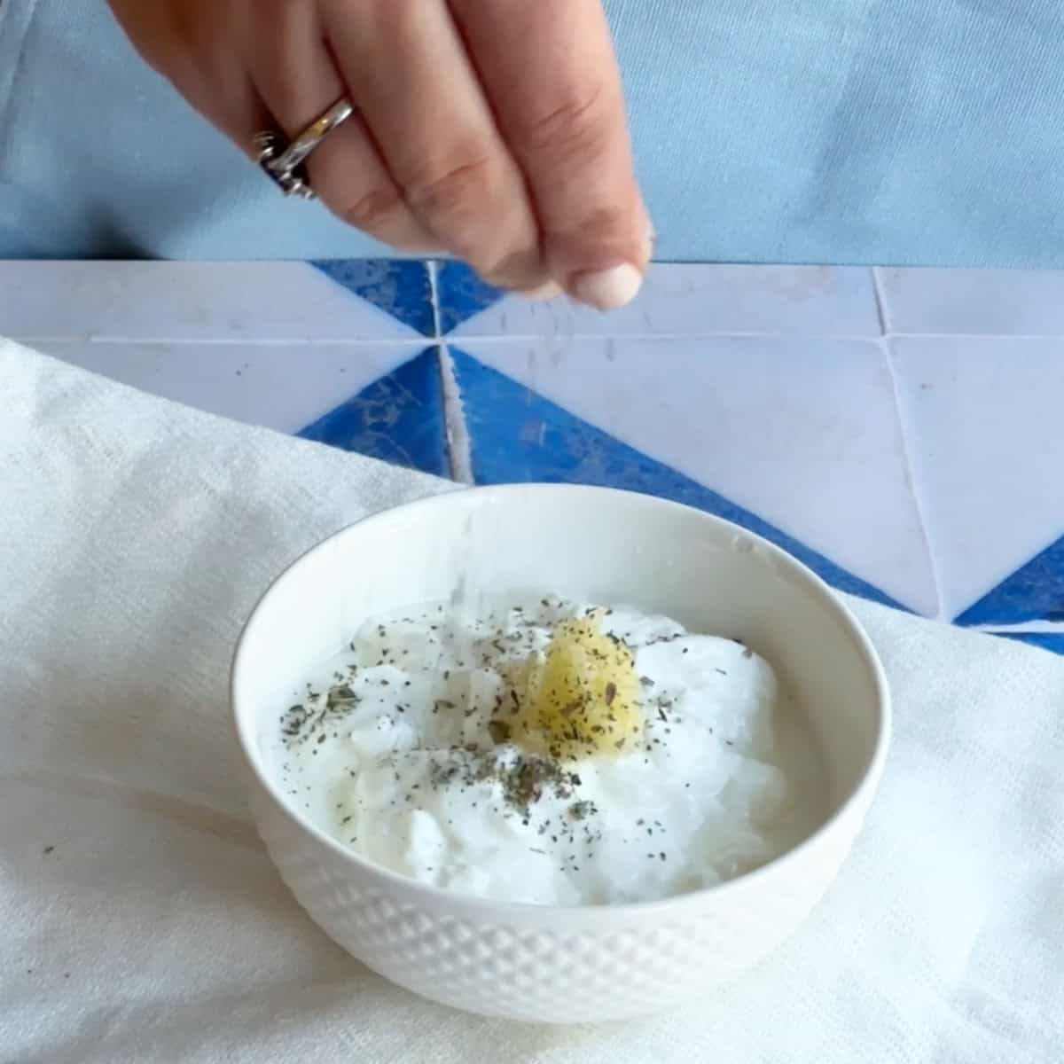 How to Make Garlic Yogurt Sauce Whole milk yogurt in a bowl with grated garlic, salt, and dried mint on top, ready to be mixed.