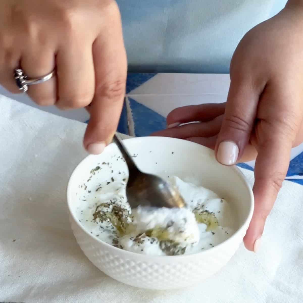How to Make Garlicky Yogurt Sauce A spoon stirring the yogurt mixture until smooth, creamy, and well-combined.