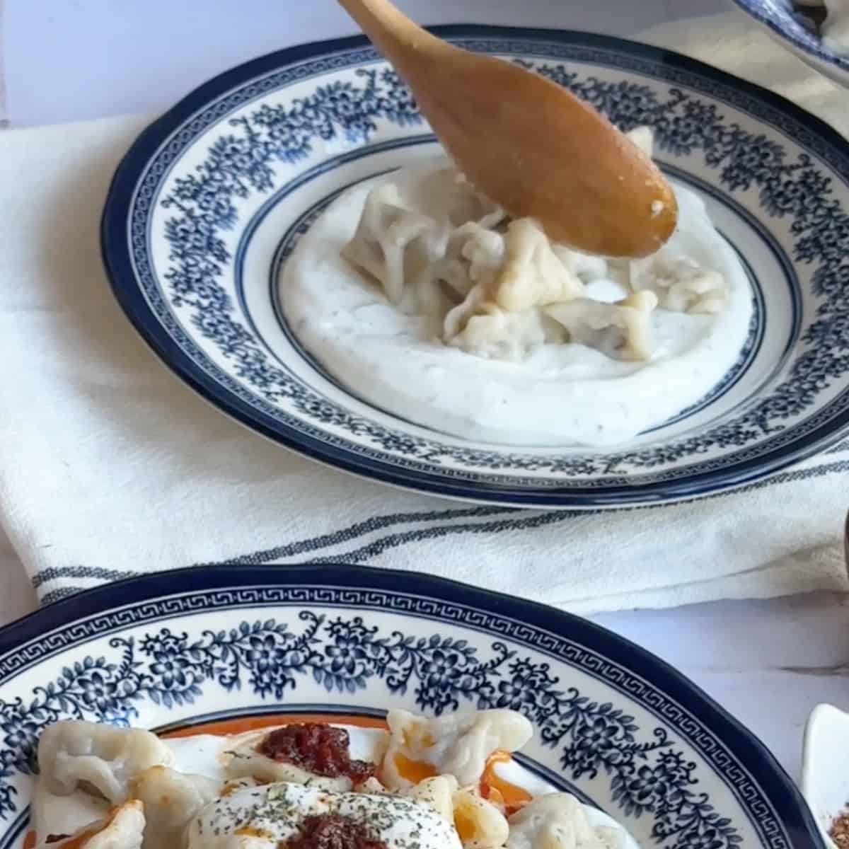 Cooked manti dumplings being carefully placed over the yogurt layer with a spoon