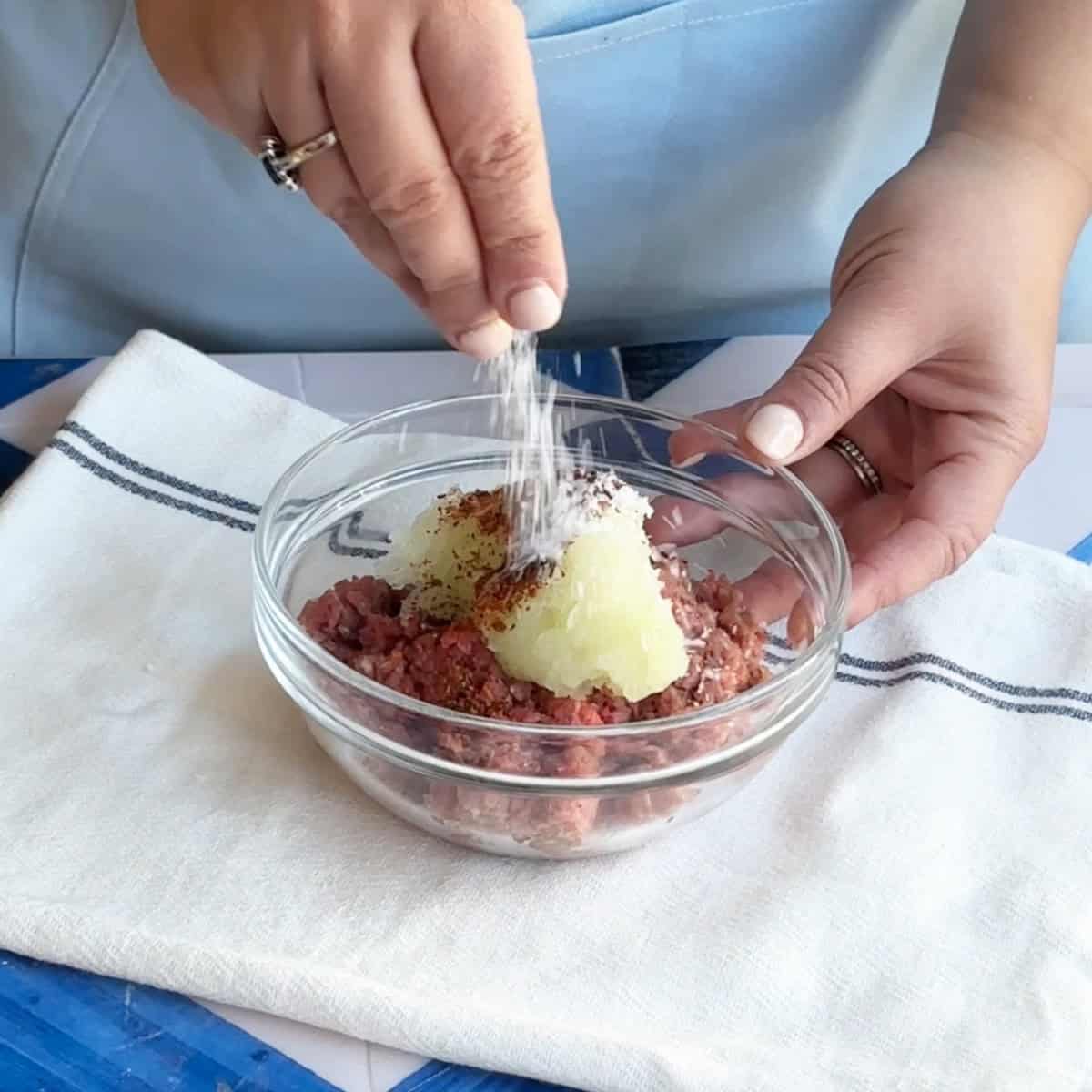 Manti Beef Filling A bowl of ground beef being mixed with grated onion, pul biber, and salt using hands.