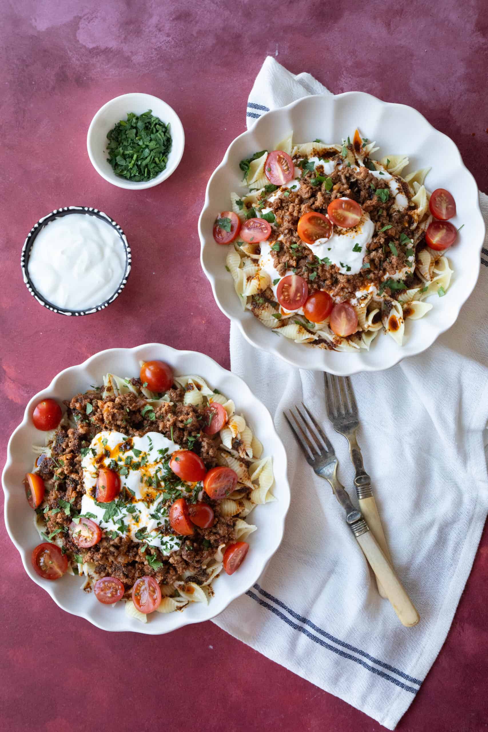two plates of pasta with ground beef and yogurt sauce, ready to be mixed for the perfect bite.