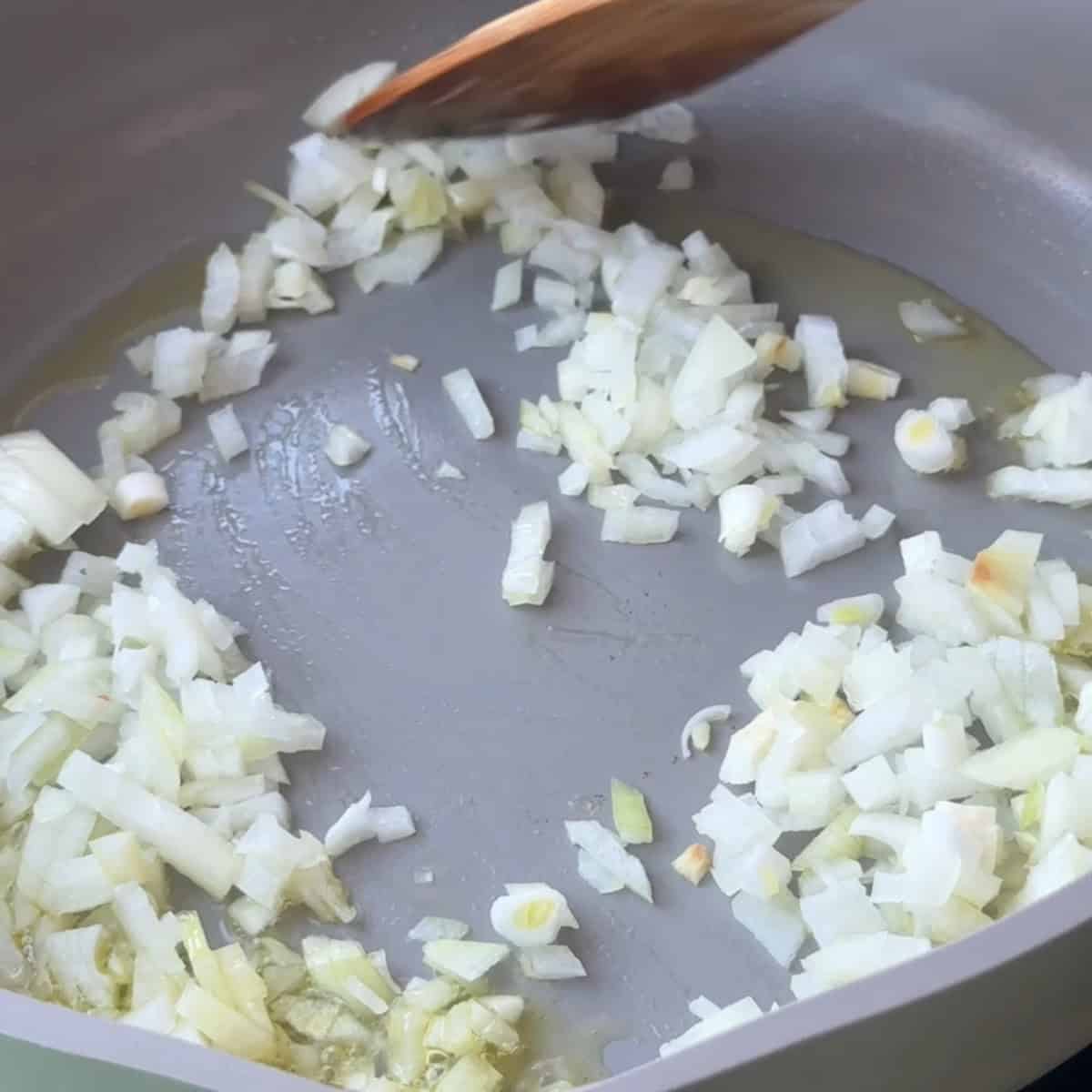 Onions and minced garlic sizzling in olive oil in a pan.