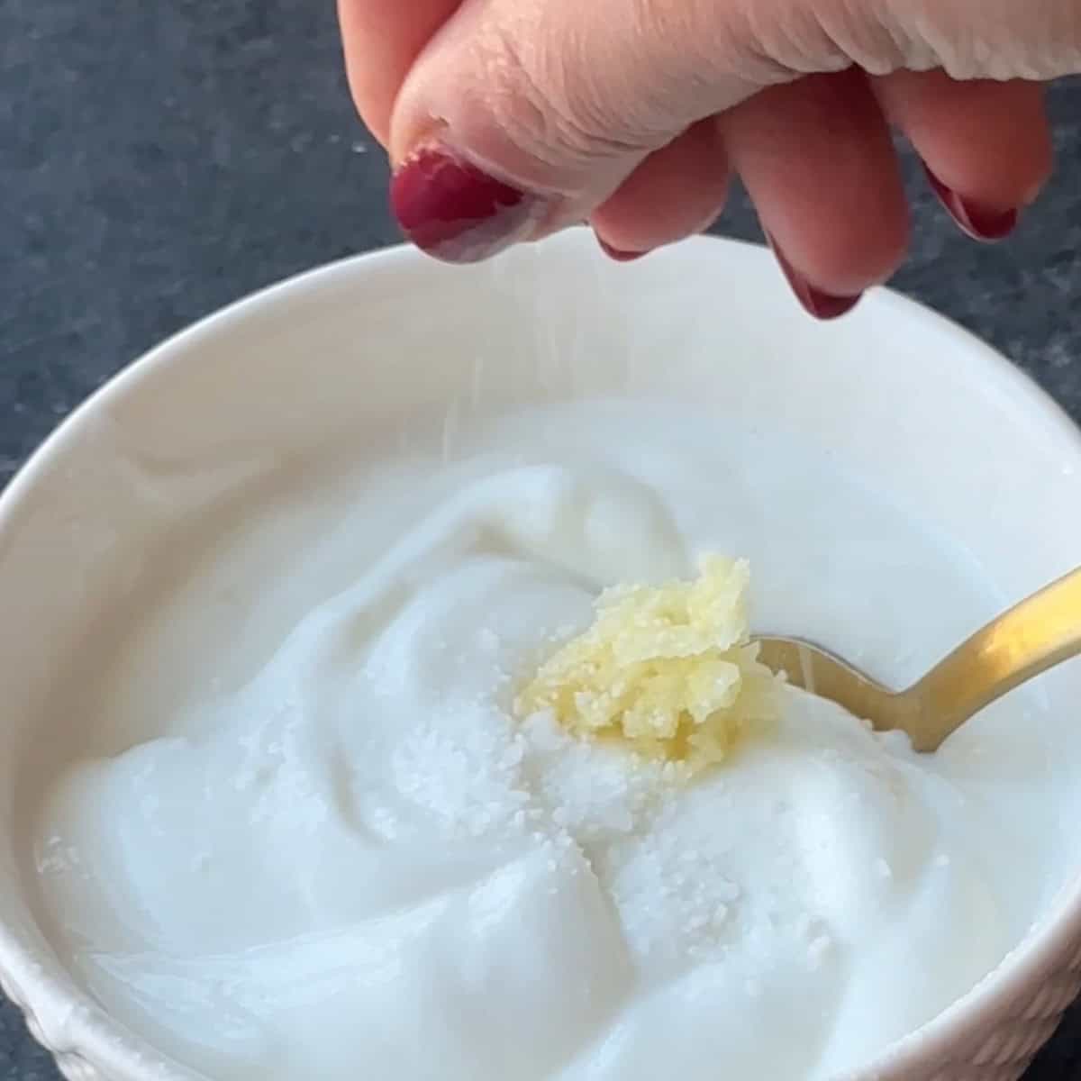 Manti Yogurt Sauce adding some salt and mixing the greek yogurt with garlic using a spoon