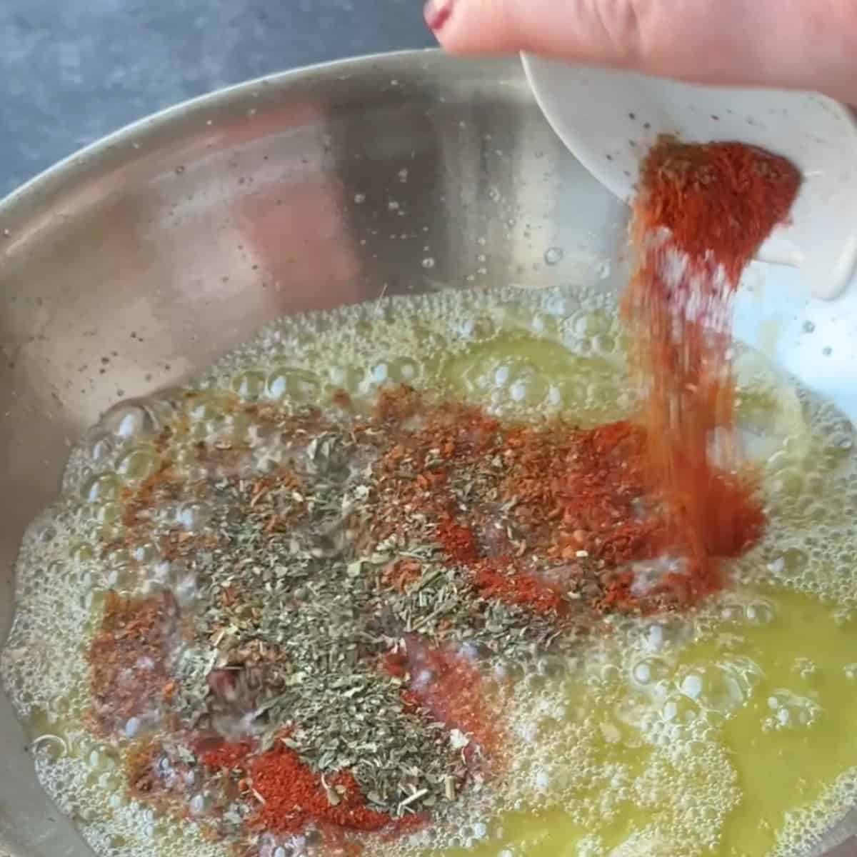 Paprika, Aleppo pepper, and dried mint being sprinkled into the butter, creating a vibrant red color.