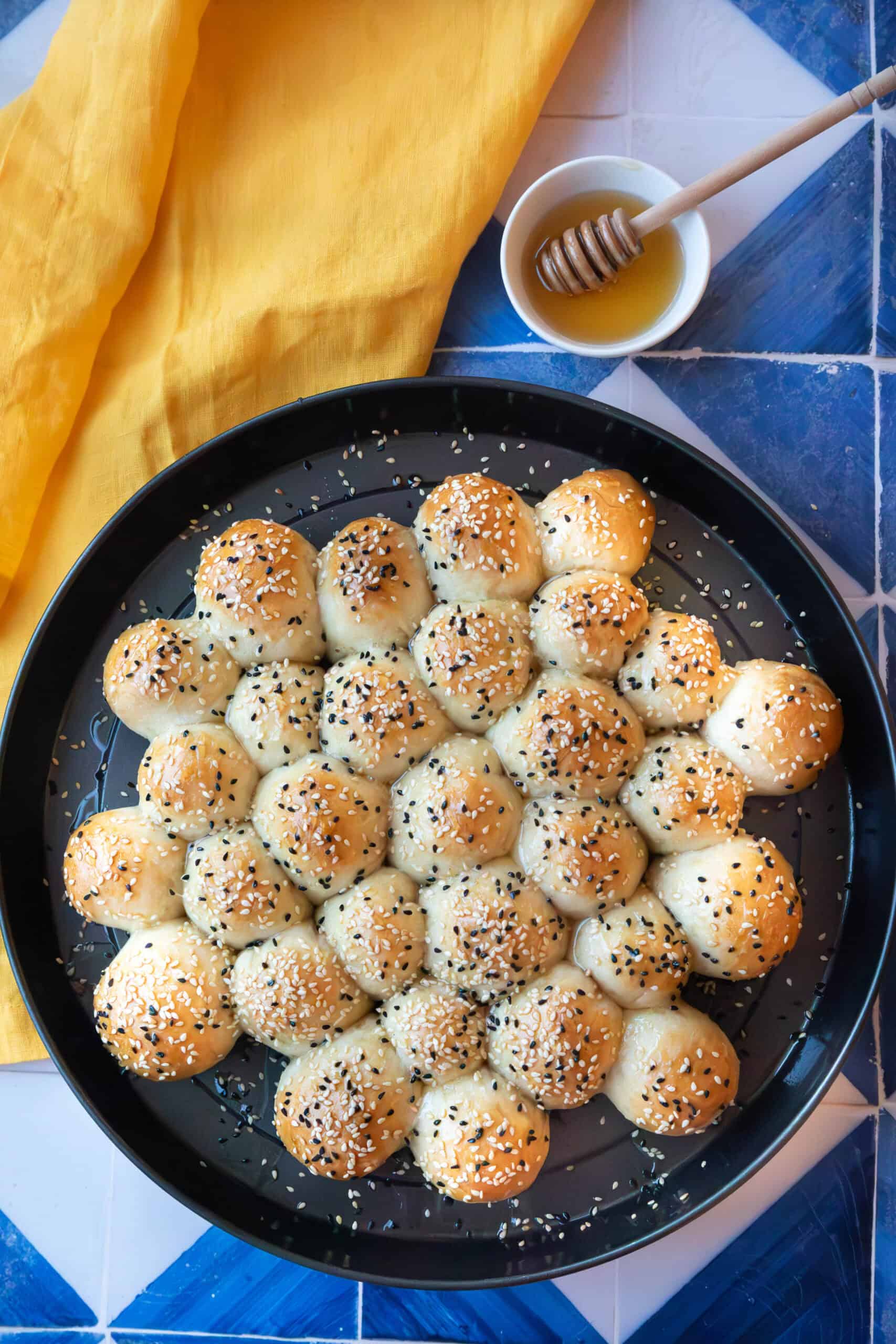 Khaliat Nahl A beautifully baked honeycomb bread in a round pan, golden brown with a glossy honey drizzle, topped with sesame and nigella seeds, ready to be served.