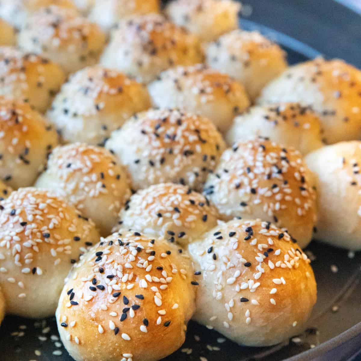 Freshly baked honeycomb bread in a round pan, golden brown with a soft, fluffy texture, topped with glistening sesame and nigella seeds.