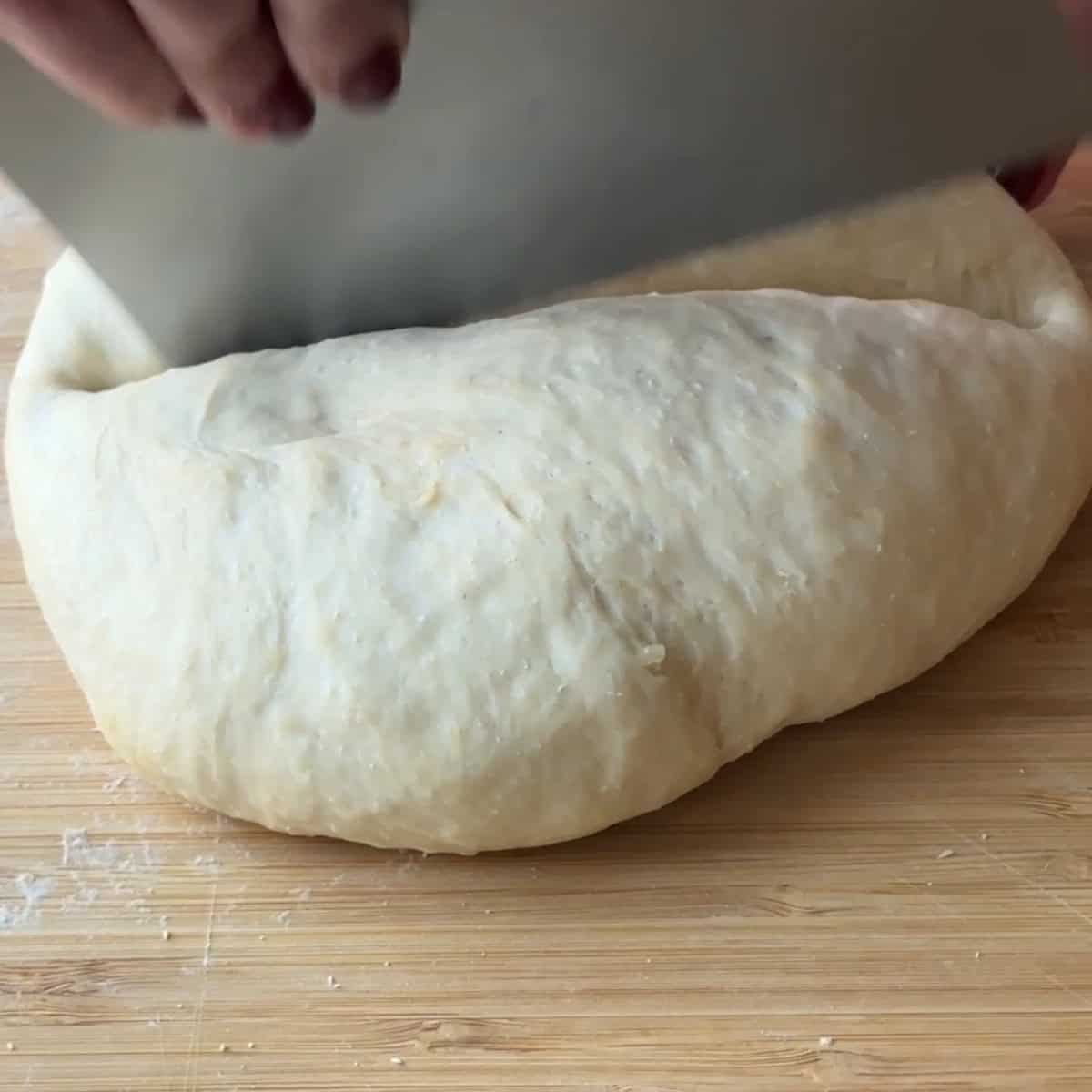 cutting the dough in half using a metal scrapper