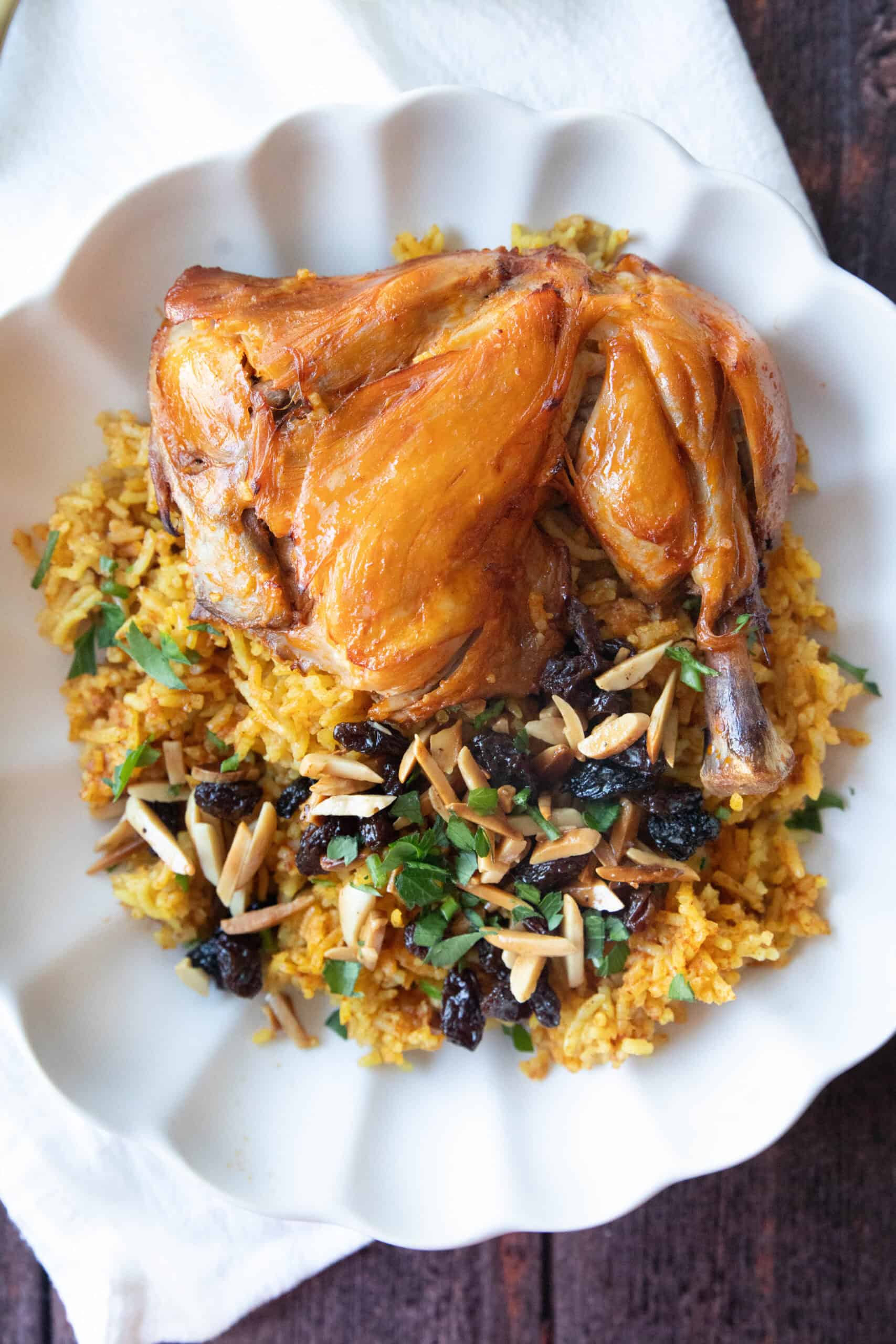 Machboos (Kabsa Chicken and Rice) Machboos or Kabsa Chicken and rice served topped with garnishes like raisin and slivered almonds in a white dish