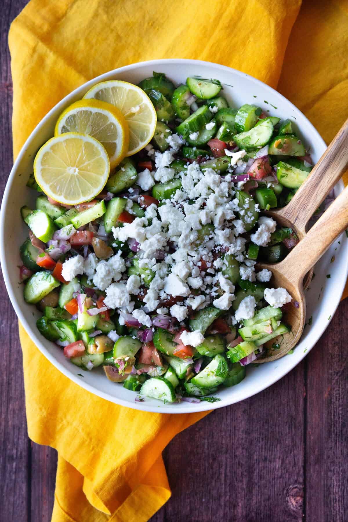 Mediterranean Cucumber Salad with Feta Cheese a top view of Mediterranean cucumber salad served in a large bowl topped with crumbled feta and served with lemon wedges