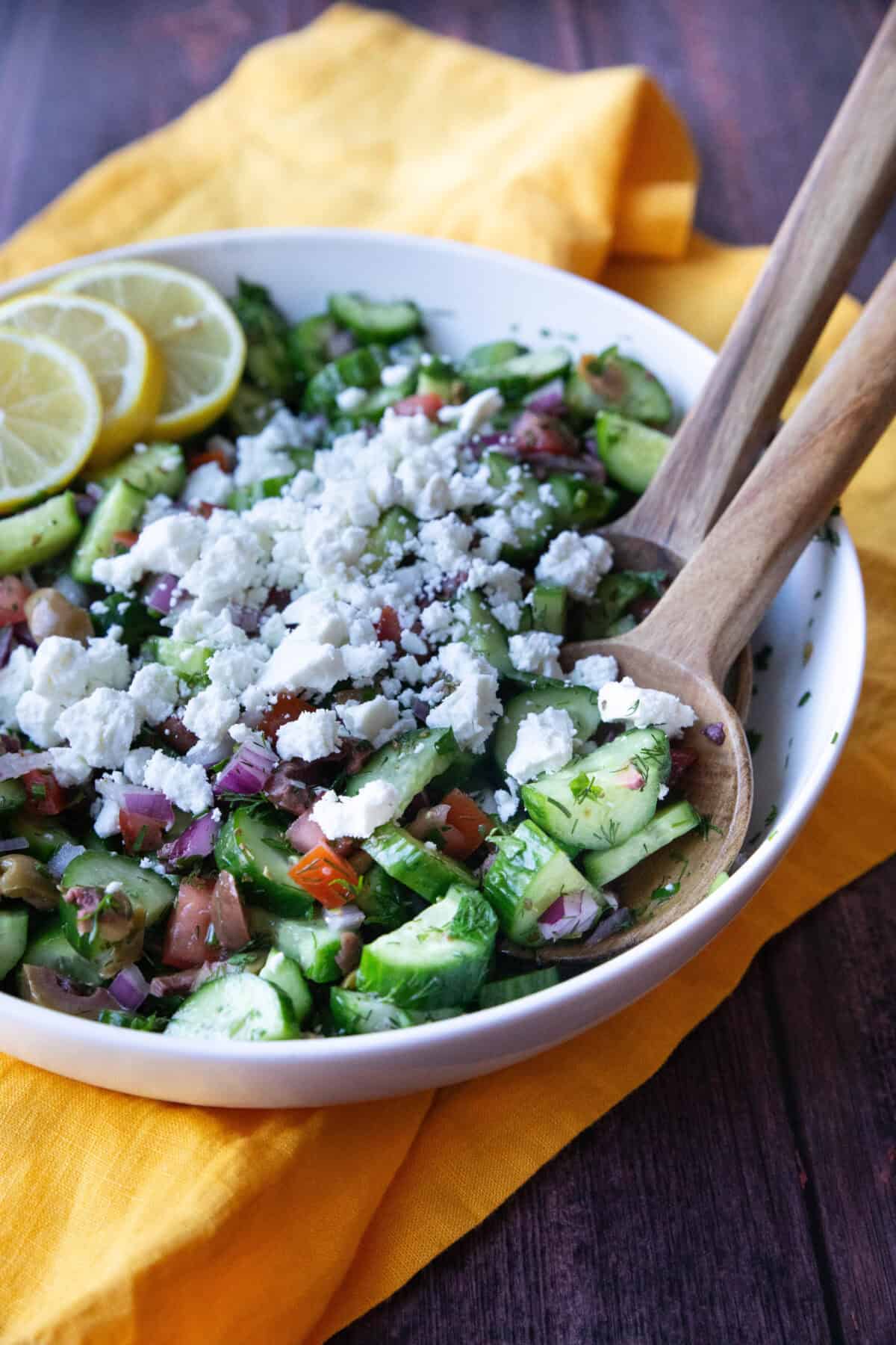 Mediterranean Cucumber Salad a side view of Mediterranean salad made with persian cucumber, roma tomatoes, red onions, fresh herbs, and olives, tangy dressing, and topped with crumbled feta