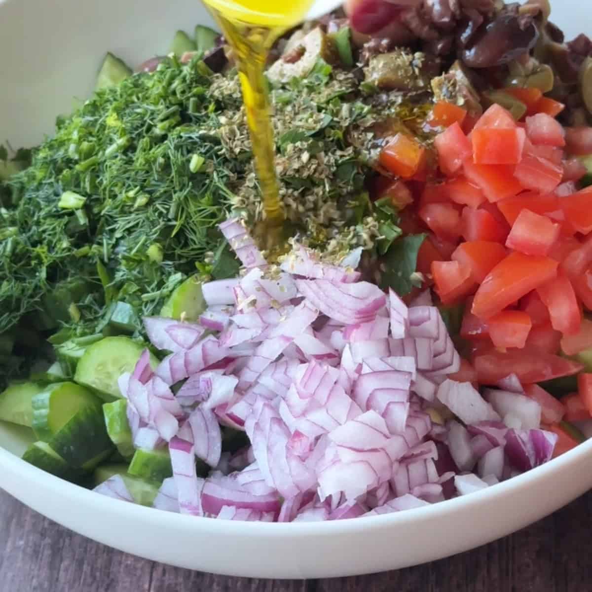 adding olive oil over Mediterranean cucumber salad ingredients