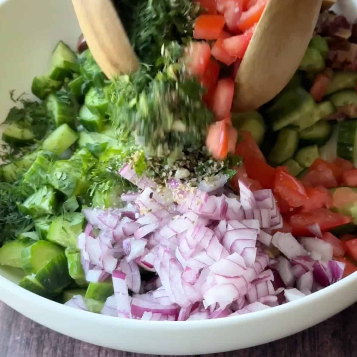 tossing the Mediterranean cucumber salad ingredients using wooden spoons