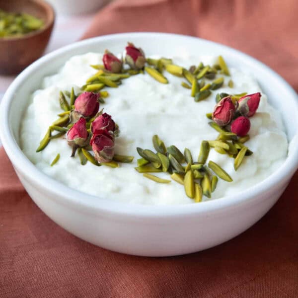A bowl of Ashta topped with pistachios and roses.
