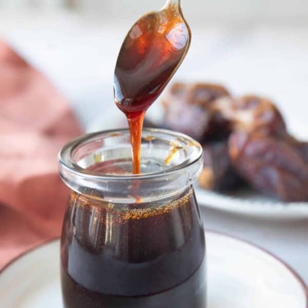 A spoon pouring date syrup into a jar.