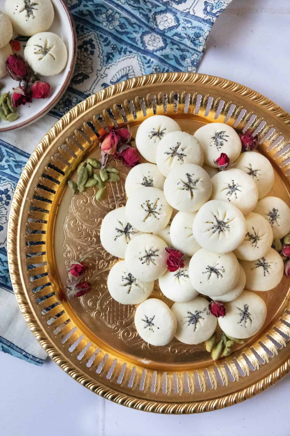Crumbly Nan-e Berenji Cookies a top shot of nan e berenji cookies served on a copper tray next to cardamom pods and rose petals