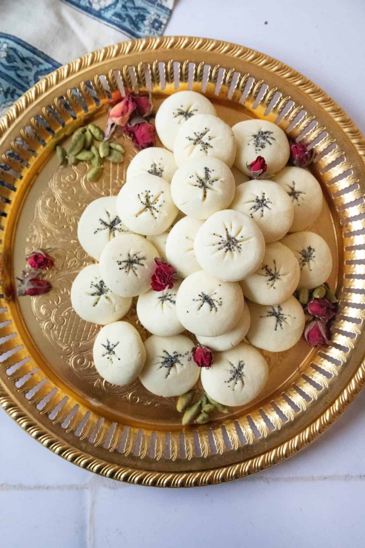 Soft Naan Berenji Cookies a top shot of nan e berenji cookies served on a copper tray next to cardamom pods and rose petals