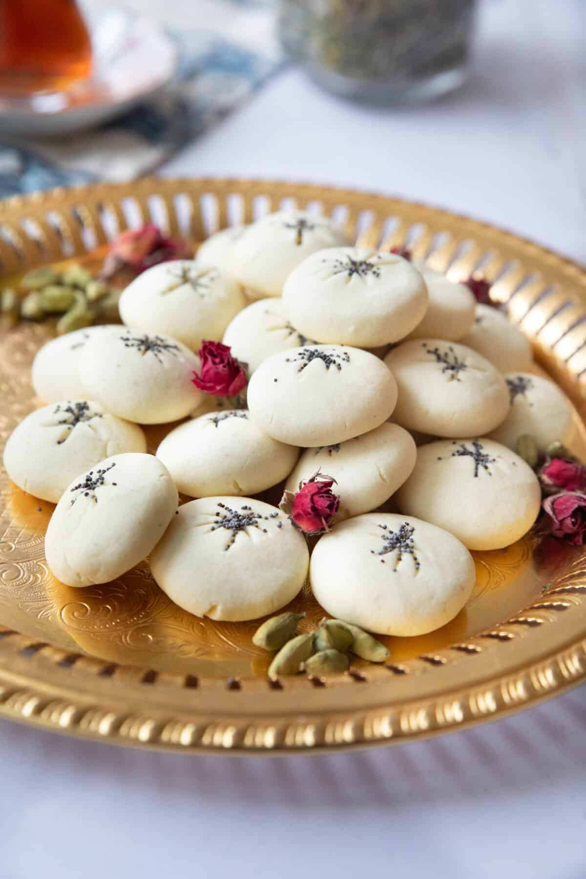 Melt-in-Mouth Naan Berenji a side shot of nan e berenji cookies topped with poppy seeds and served on a copper tray with cardamom pods and rose petals
