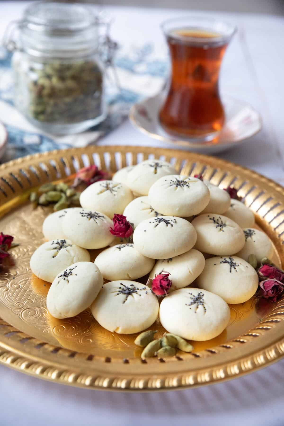 Naan Berenji - Persian Rice Cookies a side view of nan e berenji cookies served on a copper tray with cardamom pods alongside a teacup
