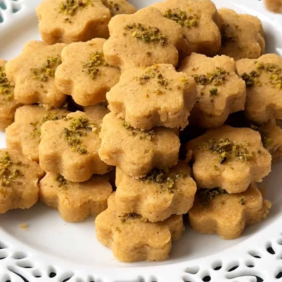 Golden Nan-e Nokhodchi cookies neatly arranged on a white plate, garnished with ground pistachios.