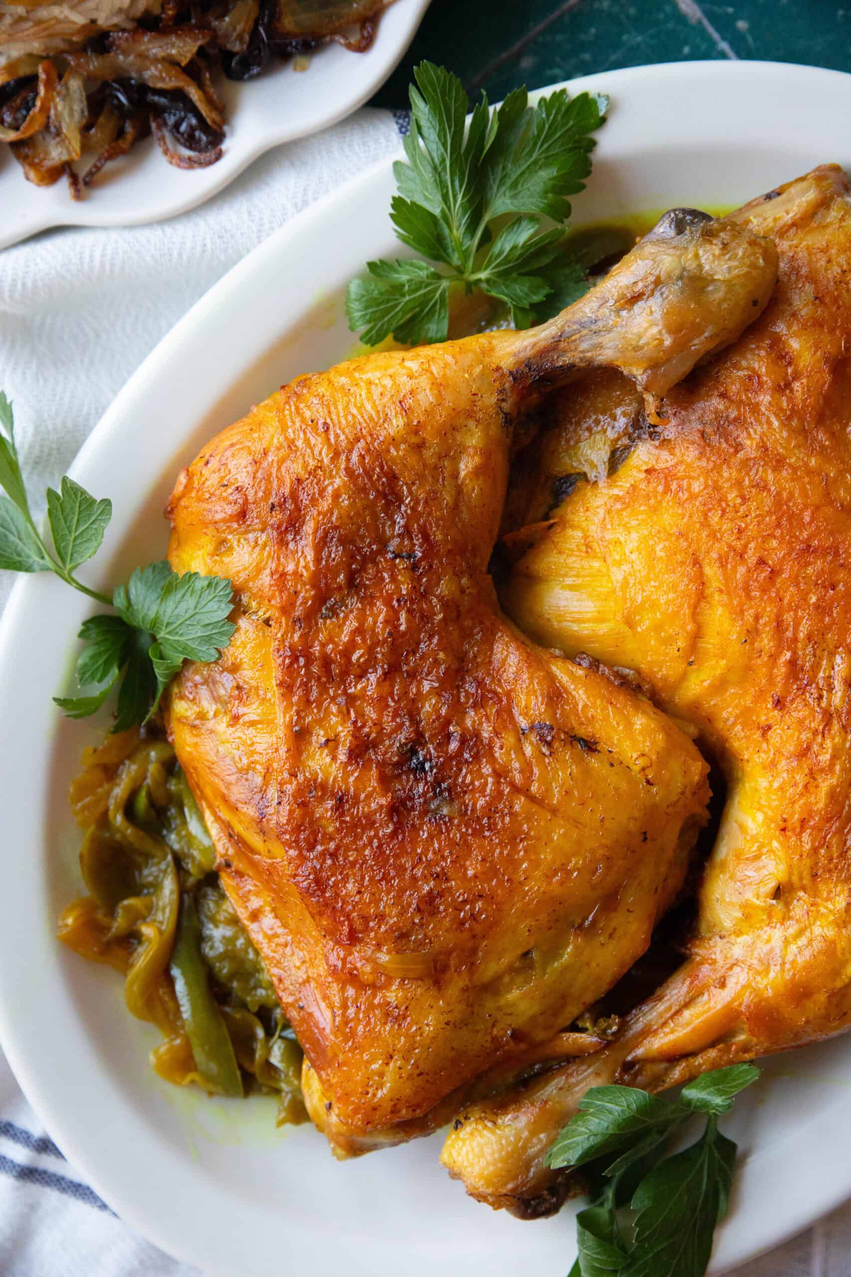 a shot of Persian saffron chicken with crispy golden skin served on a large platter with sauteed sliced onion and green blee pepper